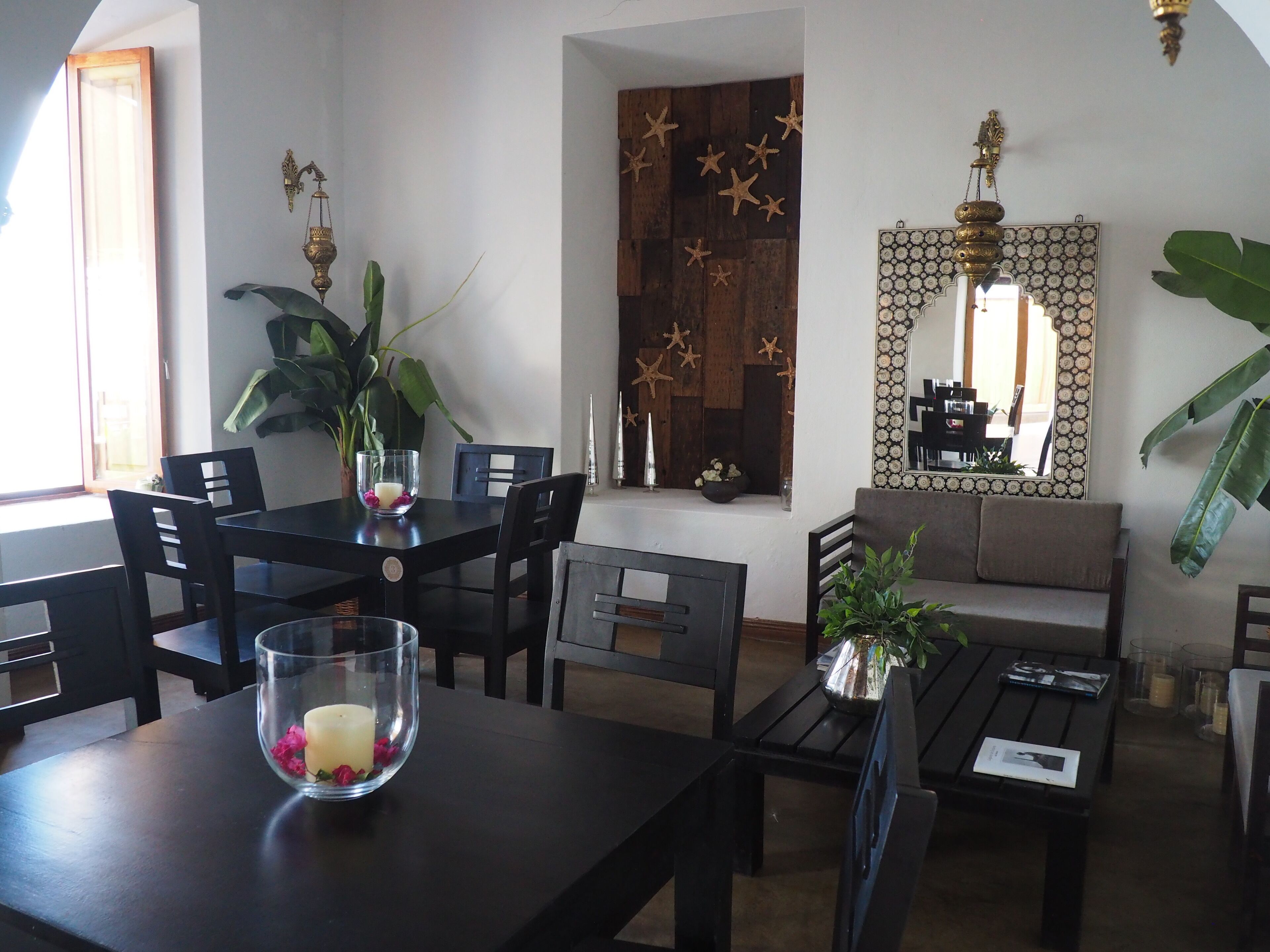 A dining area with a table, chairs, and a bowl of flowers. There is a sofa and a mirror on the wall.