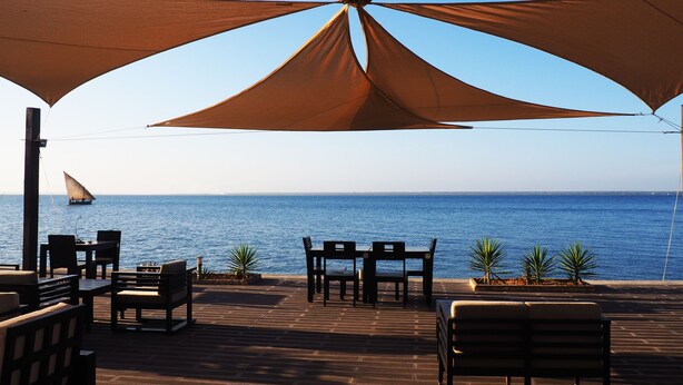 An outdoor seating area with a view of the sea, featuring a sailboat in the distance. - Feitoria Boutique Hotel (Mozambique Island)
