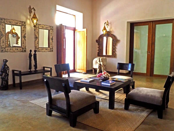 Uma sala de estar ampla com uma grande mesa de madeira, quatro cadeiras e objetos decorativos, incluindo uma estátua e uma tigela com flores.