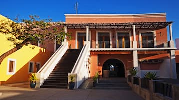 Um edifício com escadaria que dá para uma varanda, céu claro e plantas em vasos.