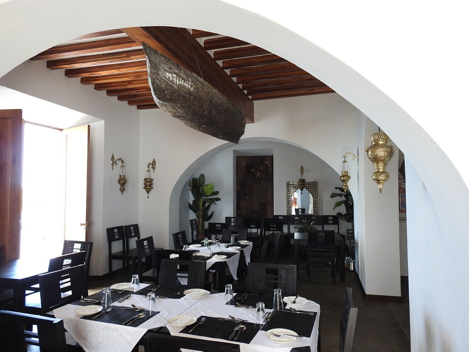 Restaurante com várias mesas preparadas para refeições, vigas de madeira no teto e detalhes decorativos nas paredes.