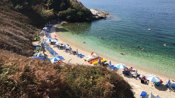 A beach with clear waters, umbrellas, and beach chairs. - Philippos Apartments (Corfu)