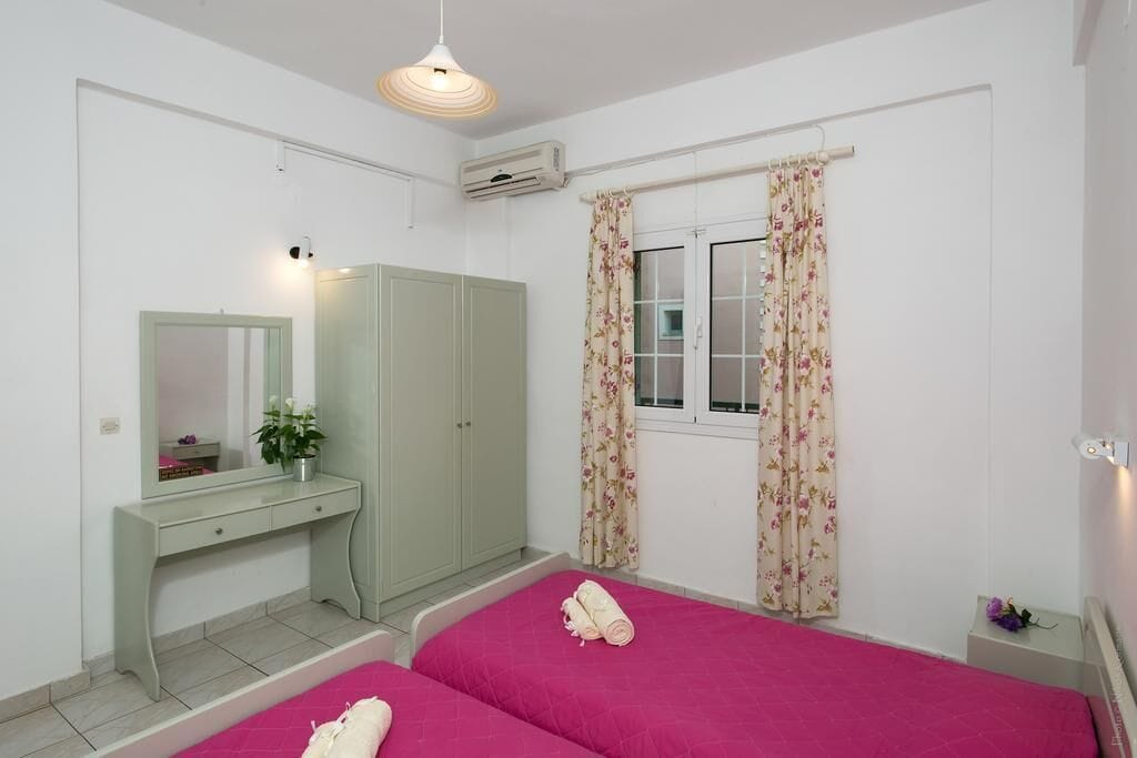 A bedroom with two beds, a desk, a wardrobe, and a window with floral curtains.