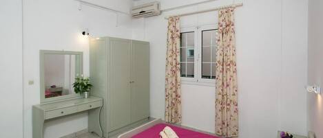 A bedroom with two beds, a desk, a wardrobe, and a window with floral curtains.