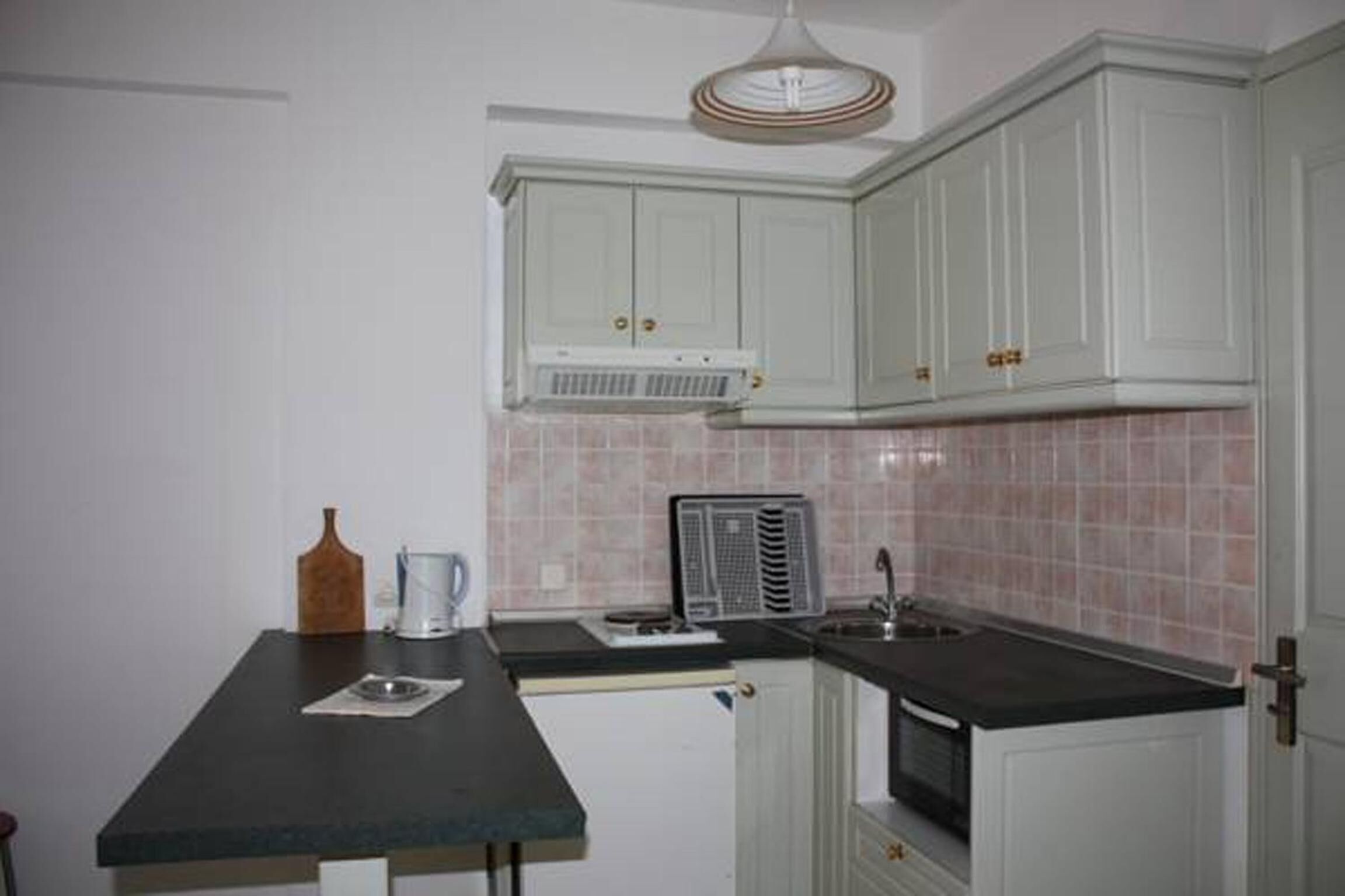 A compact kitchen with white cabinets, a black countertop, and a pink-tiled backsplash.