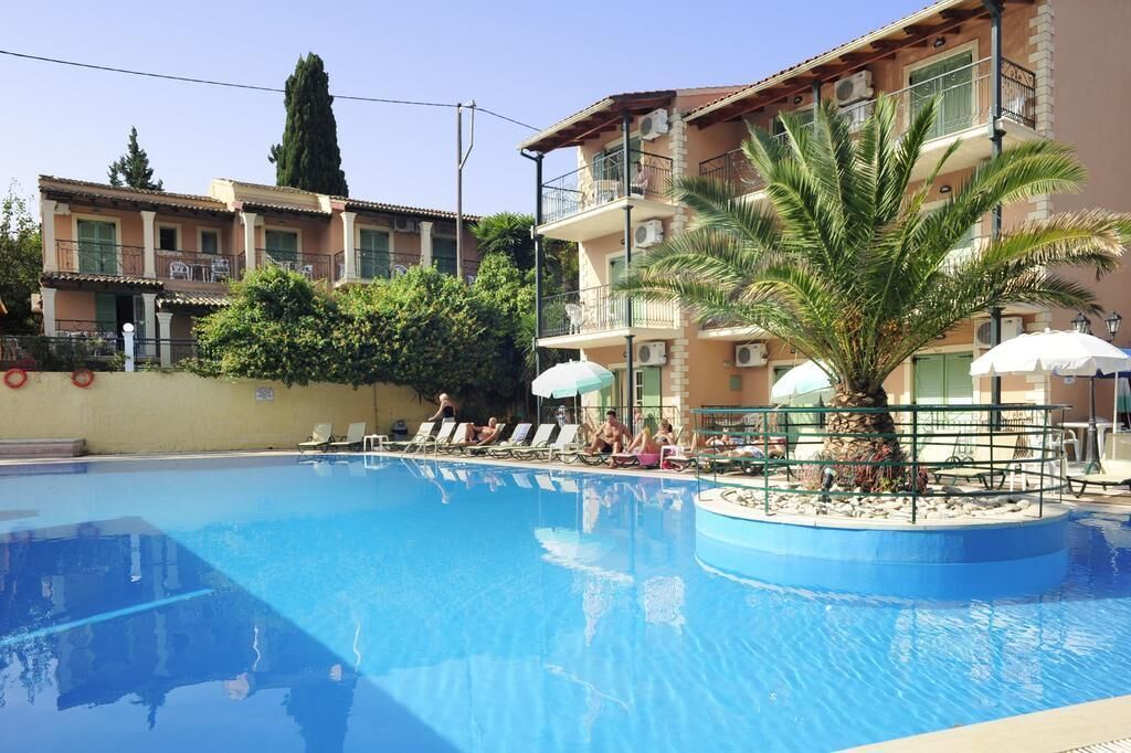 A swimming pool with lounge chairs and umbrellas, surrounded by multi-story buildings with balconies and air conditioning units.