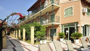 A hotel with outdoor seating, a covered walkway, and a building with multiple balconies. - Philippos Apartments (Corfu)