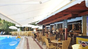 An outdoor pool area with wicker chairs and tables, a bar, and umbrellas. - Philippos Apartments (Corfu)