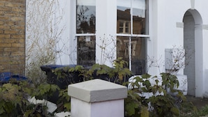 A two-story house with a white facade, a brick chimney, and a small porch with a white balustrade. - Sail Away - 2-Bed Apartment by the Beach (Whitstable)