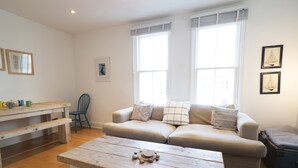 A cozy living room with a wooden coffee table, a beige sofa, and a blue chair. - Sail Away - 2-Bed Apartment by the Beach (Whitstable)