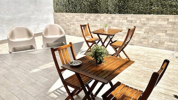 Eine Terrasse im Freien mit Holztischen und -stühlen, einem Blumentopf und einer Steinwand mit Bepflanzung.