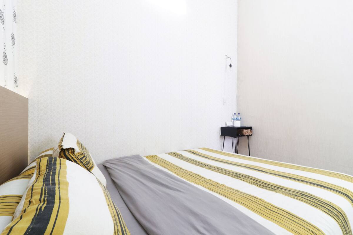 A hotel room with a bed, a nightstand, and a wall socket.