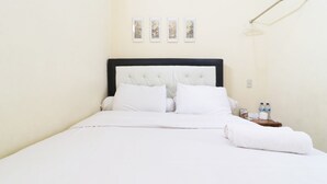 A neatly made bed with white linens, a bedside table with bottled water, and a wall-mounted light fixture.