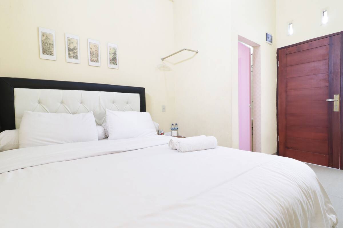 A neatly made bed with white linens, a wooden headboard, and a nightstand with two bottles.