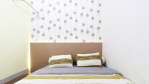 A neatly made bed with striped bedding and two pillows, a wooden headboard, and a patterned curtain.
