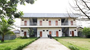 A two-story building with a central entrance, a motorcycle parked outside, and a well-maintained lawn with white flowers.