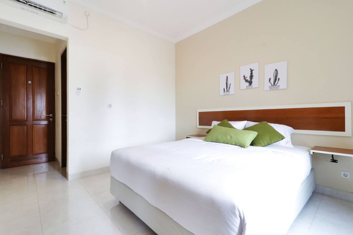 A hotel room with a large bed, a wooden wardrobe, and a nightstand with a lamp.