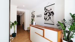 A reception desk with a wooden top and white paneling, flanked by potted plants. - Nikara Residence Syariah (Jakarta)