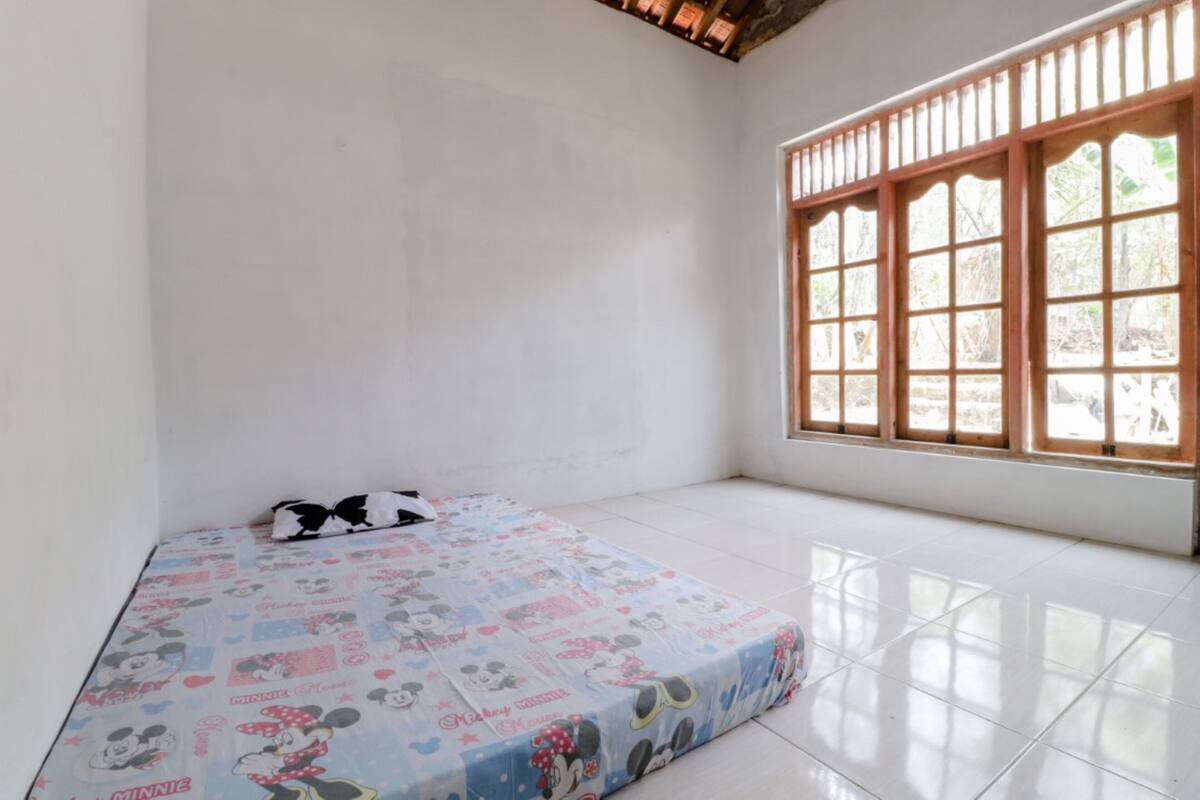 A room with a bed covered in Minnie Mouse-themed bedding, a window with wooden bars, and a tiled floor.