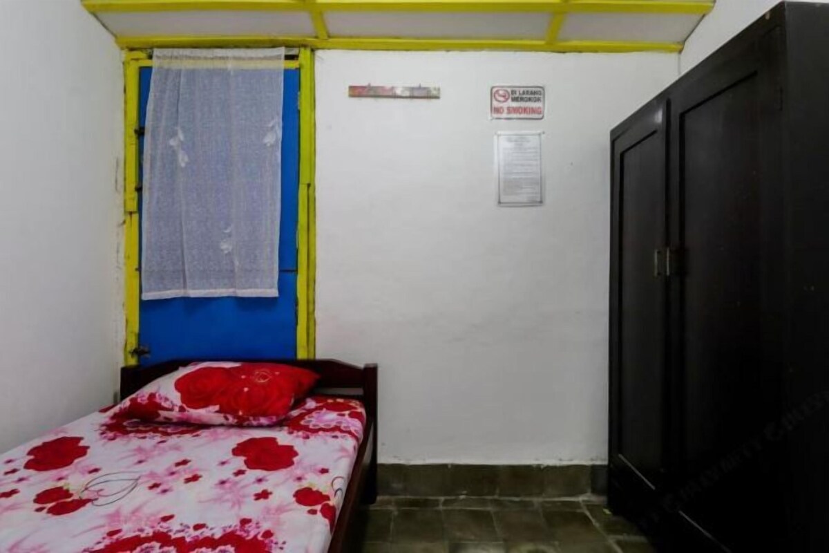 A small room with a bed, a wardrobe, and a window with a curtain.