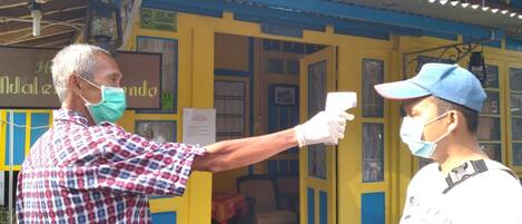 A person conducting a temperature check on another individual at a yellow building with blue accents.