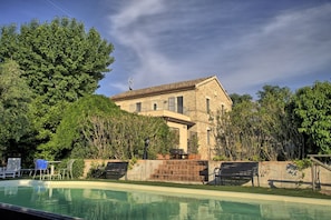 A pool area with a stone building, outdoor furniture, and lush greenery.