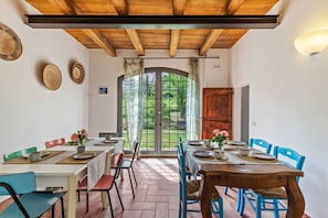 A dining area with a wooden ceiling, a large window with curtains, and a view of greenery outside.