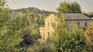 A stone building with a tiled roof, surrounded by greenery and a hilly landscape in the background. - Large historic villa with pool, panoramic views surrounded by greenery (Ostra)