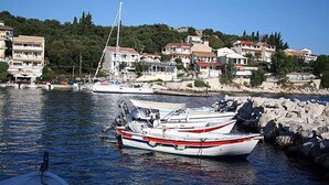 A marina with several boats docked, surrounded by residential buildings and a hilly backdrop. - Kipos Apartments (Corfu)
