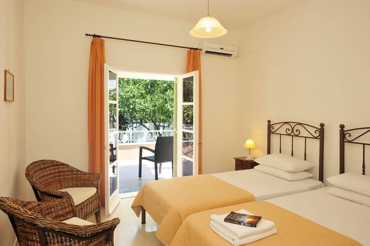 A hotel room with two beds, a wicker chair, a balcony with a view, and an air conditioning unit.