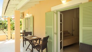 A room with a bed, a table with chairs, and a balcony with a railing. - Kipos Apartments (Corfu)