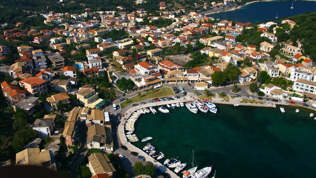 An aerial view of a coastal town with a marina, houses, and a hilly backdrop. - Kipos Apartments (Corfu)