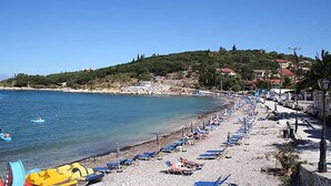 A beach with rows of blue lounge chairs and a few yellow kayaks. - Kipos Apartments (Corfu)