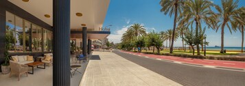 Un hotel con terraza al aire libre, palmeras y vistas a la playa.
