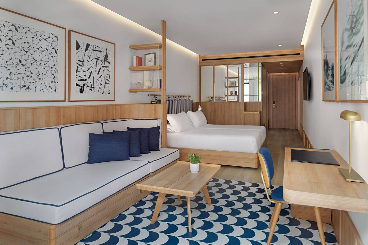 A modern hotel room with a sofa, a bed, a small table, and a TV.