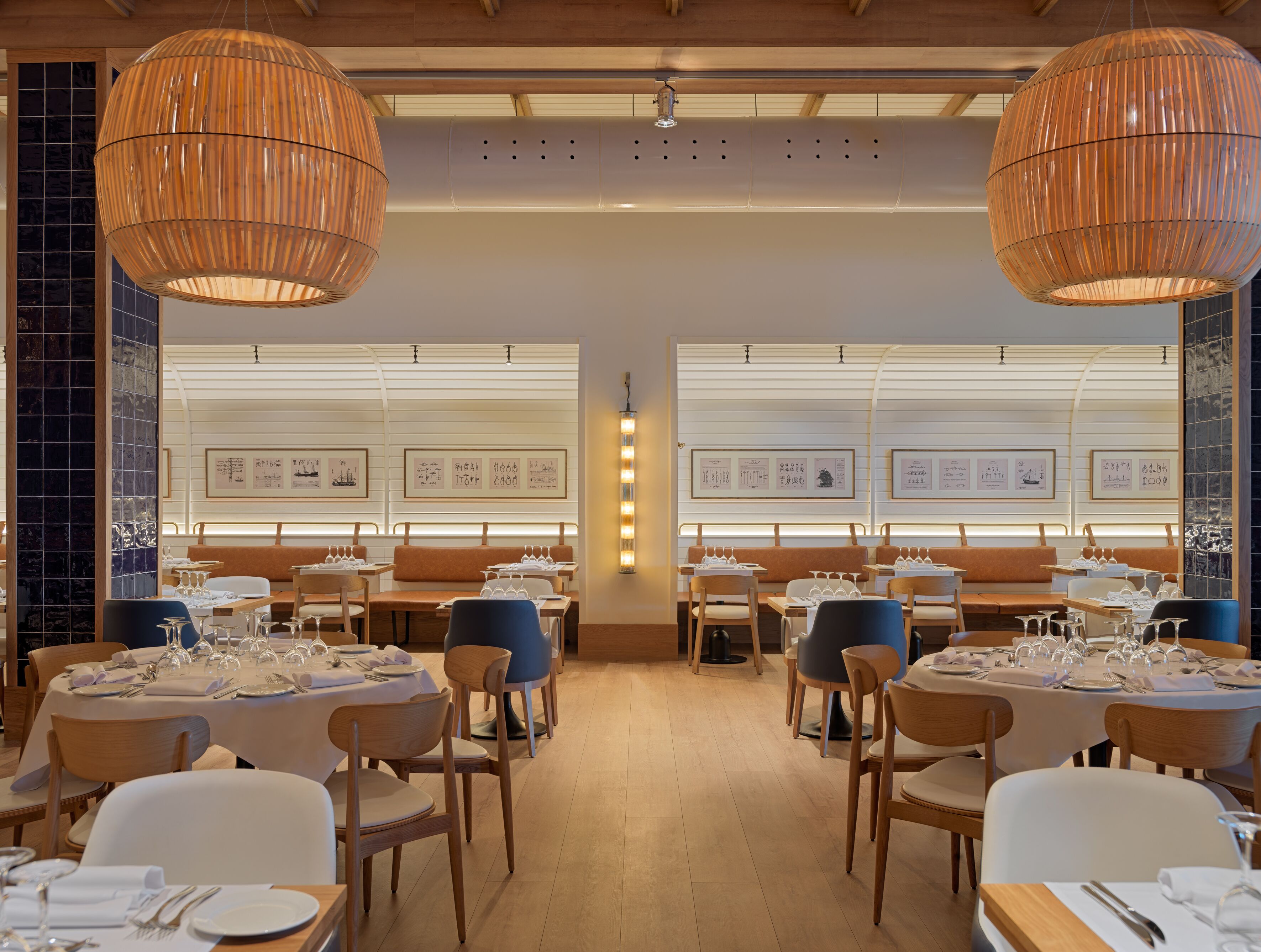 Ein Restaurant mit Holztischen und -stühlen, gerahmten Kunstwerken an den Wänden und großen Pendelleuchten.
