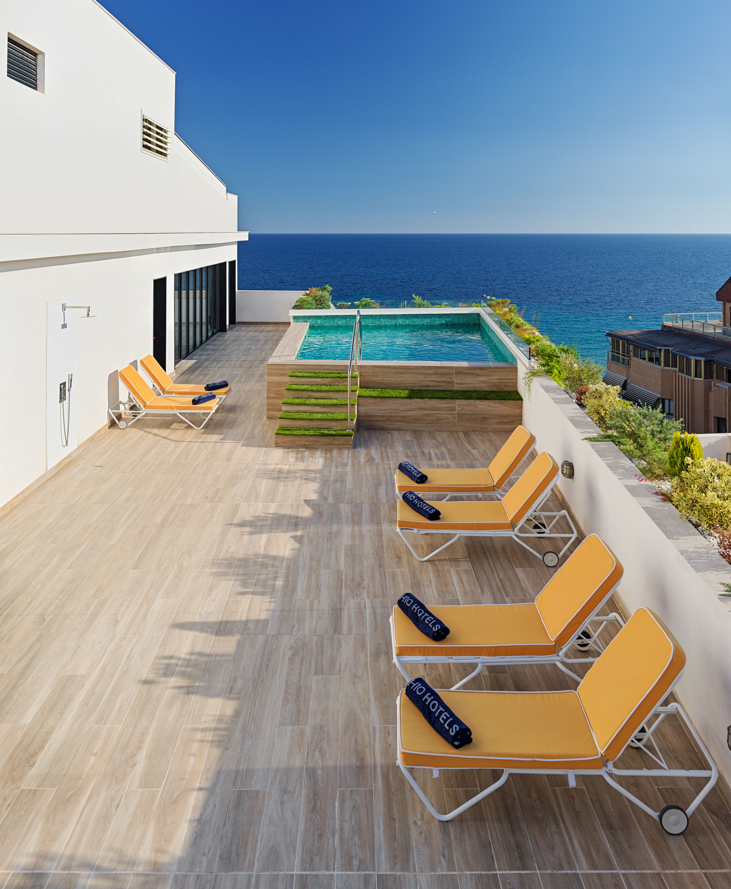A rooftop pool area with sun loungers, a small pool, and a view of the ocean.