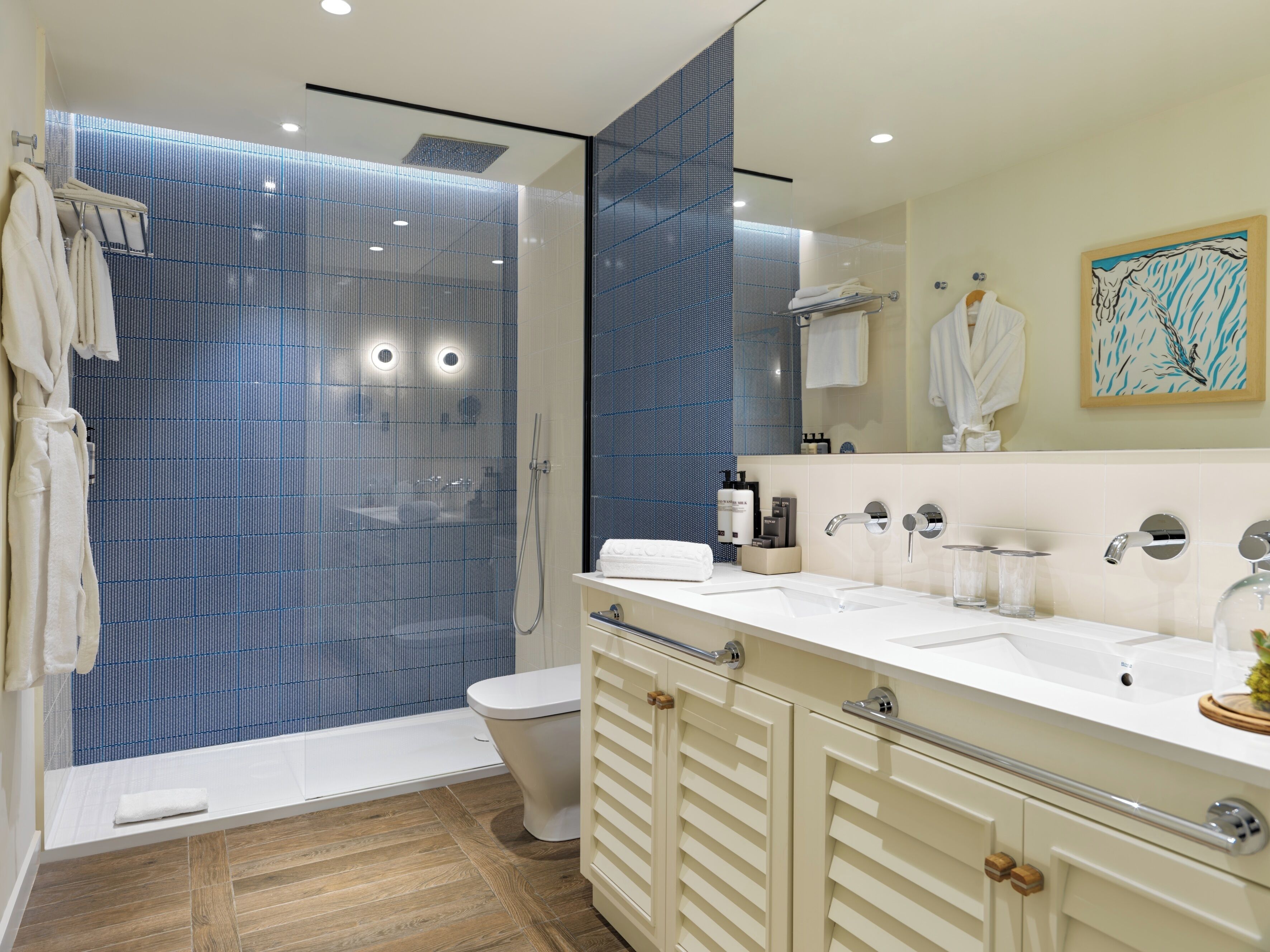 A modern bathroom with a glass-enclosed shower, a white sink with a mirror, and a wooden floor.