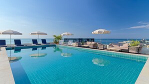 Zona de piscina con sillones de descanso y sombrillas, cielo despejado y vista al océano.