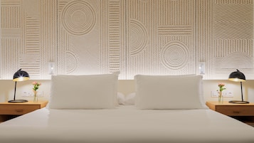 Una cama bien hecha con dos almohadas, una mesita de noche con una lámpara y un florero, y una pared con textura.