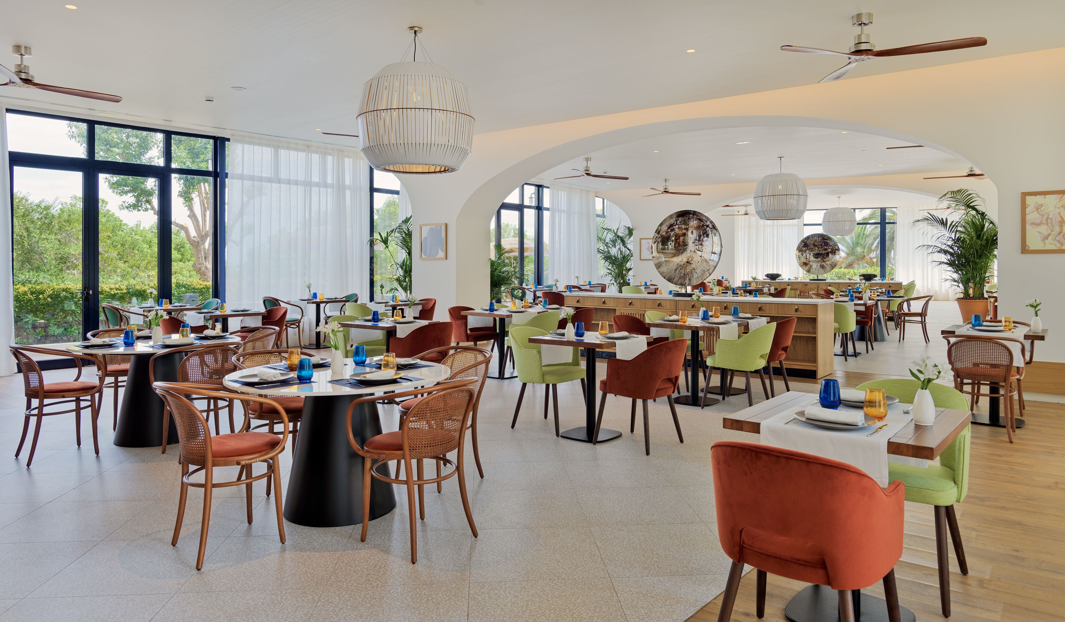 A spacious dining area with multiple tables and chairs, large windows, and ceiling fans.