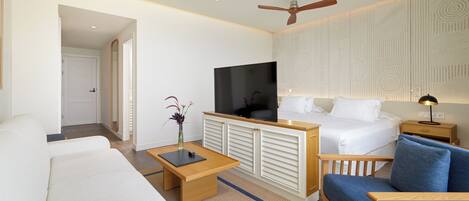 A hotel room with a bed, a sofa, a chair, a TV, and a ceiling fan.