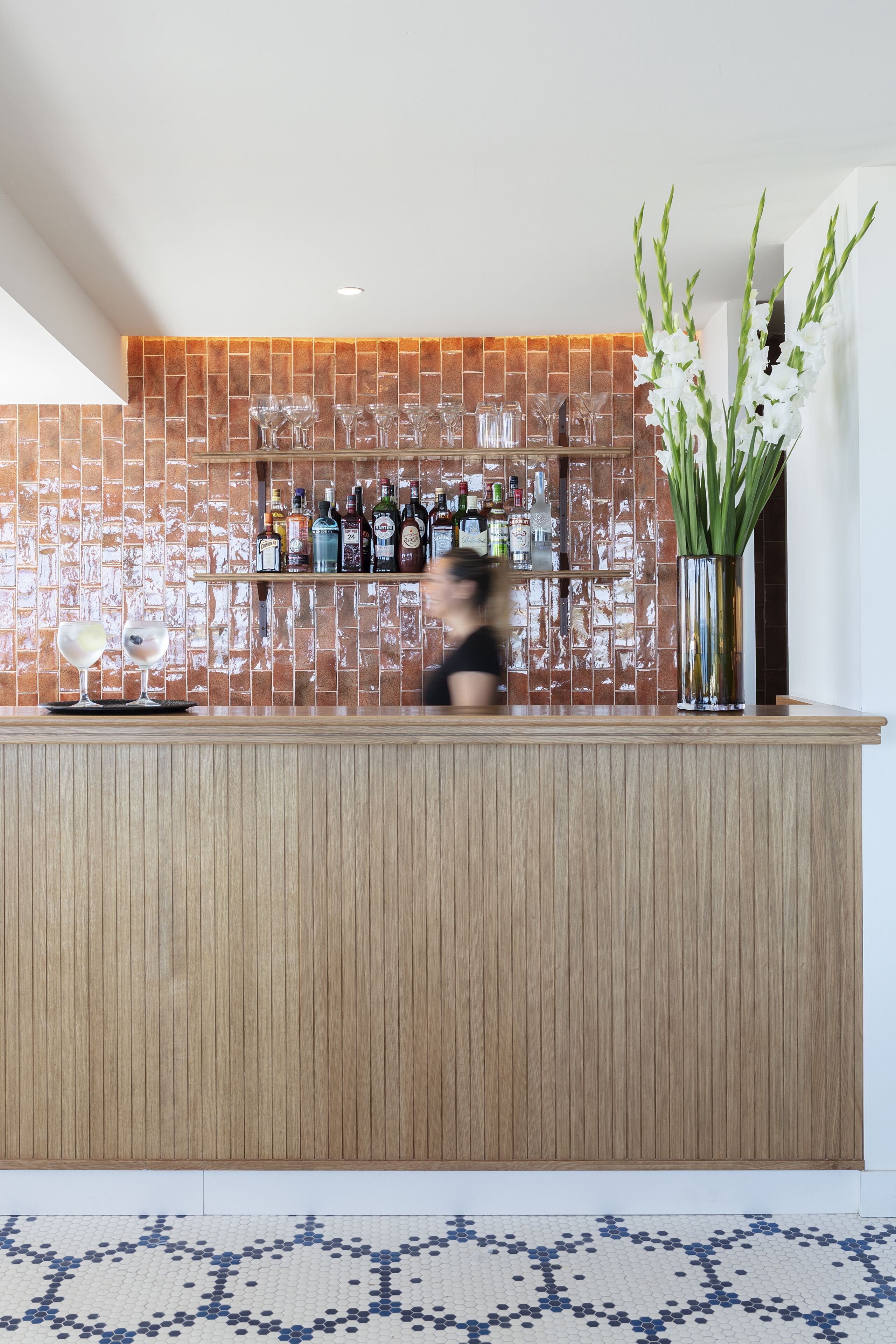 Zona de bar con salpicadero de azulejos, mostrador de madera y un jarrón con flores blancas.