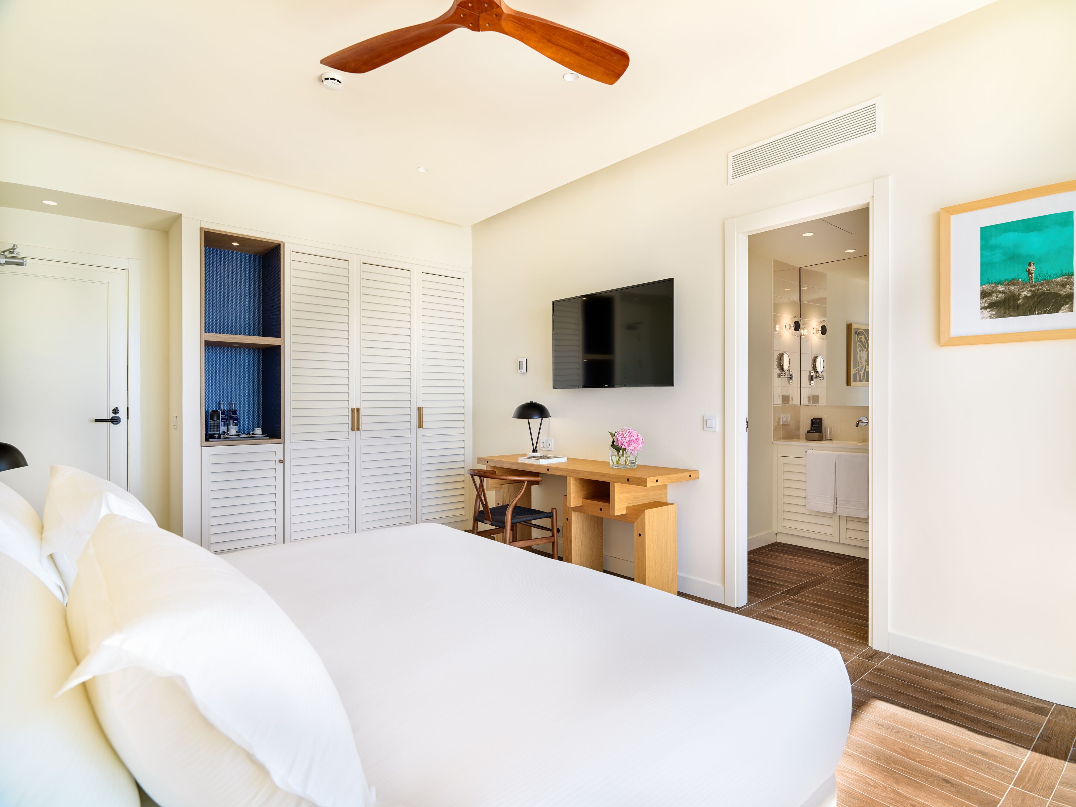 Een slaapkamer met een bed, bureau, televisie, kast en een badkamer door een geopende deur zichtbaar.