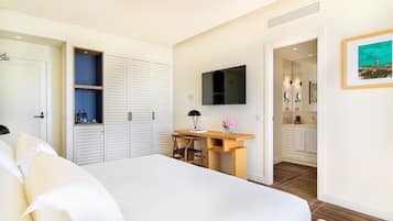 Een slaapkamer met een bed, bureau, televisie, kast en een badkamer door een geopende deur zichtbaar.