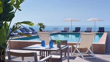 Un espace aménagé au bord de la piscine, avec des chaises longues, une table où sont servis des boissons et des parasols offrant une vue sur l’océan.