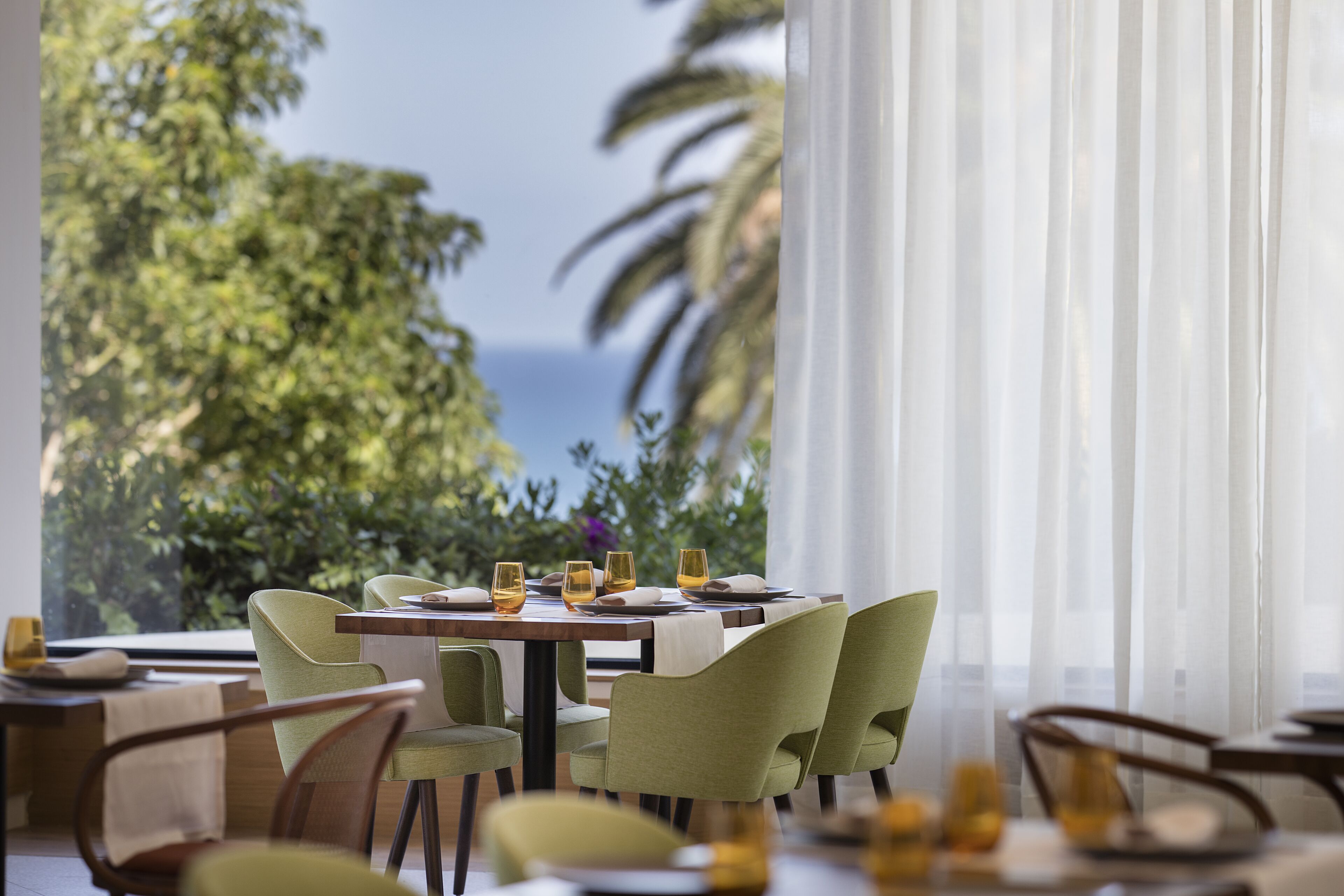 Un coin repas avec une table dressée pour quatre personnes, des chaises et une vue sur la mer grâce à de grandes fenêtres.