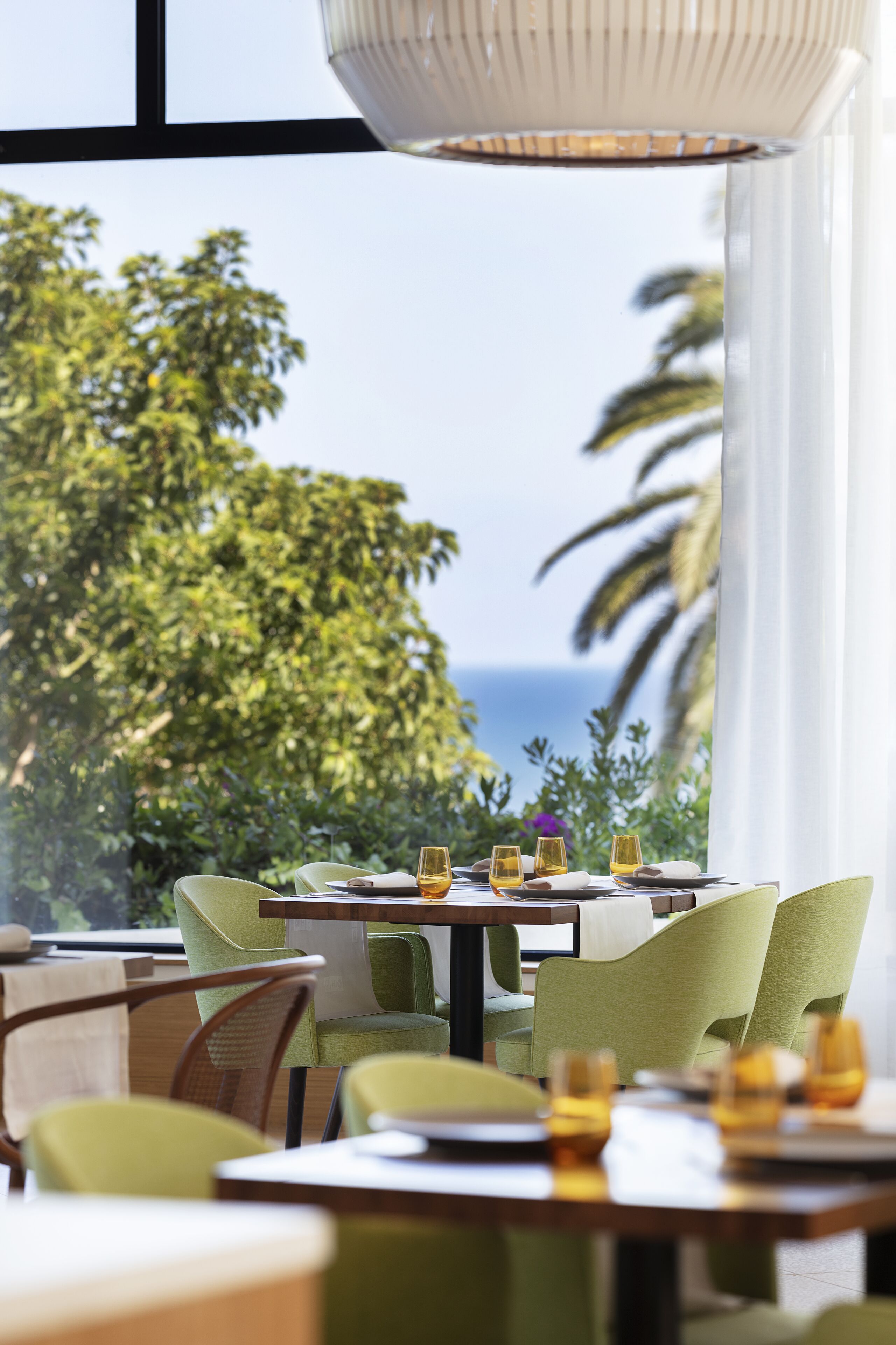A dining area with tables set for four, chairs, and a view of the ocean through large windows.