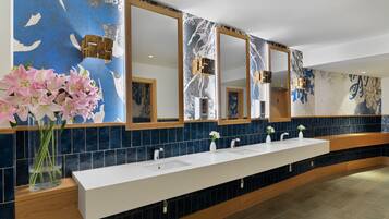A long, white bathroom vanity with three sinks, large mirrors, and a blue-tiled backsplash.