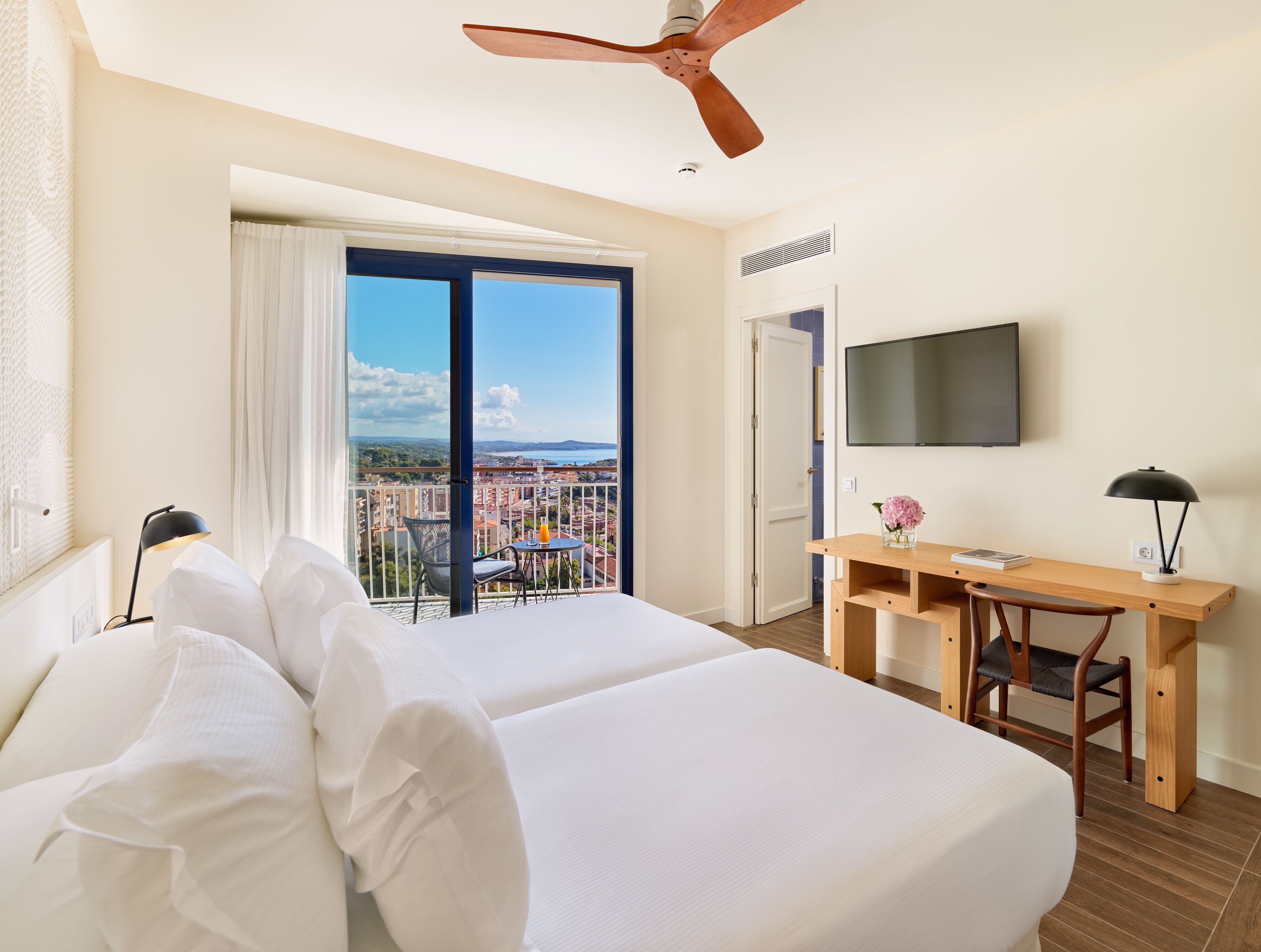 A hotel room with a bed, a desk, a chair, a TV, and a balcony with a view.
